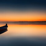 A solitary boat flows on a calm lake during a sunset with a Scorpio New Moon casting its glow in the sky.