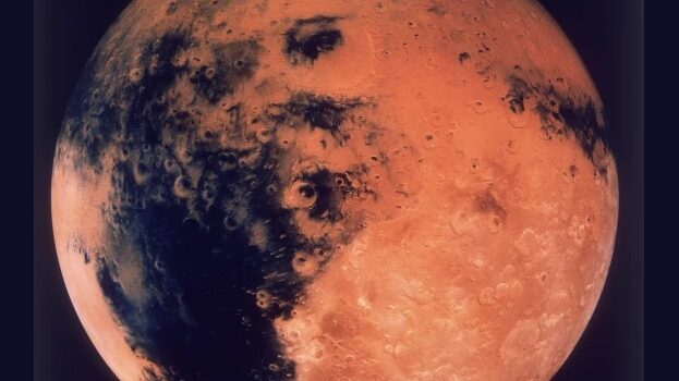 Image of the planet Mars in retrograde, showcasing its reddish-orange surface with visible craters and dark patches, symbolizing cosmic conflict and flux.